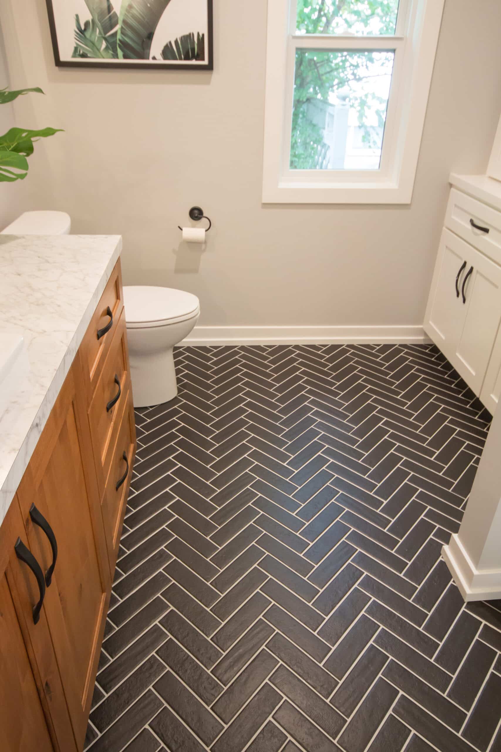 Bathroom with black herringbone tile floor, white walls, and wooden vanity.