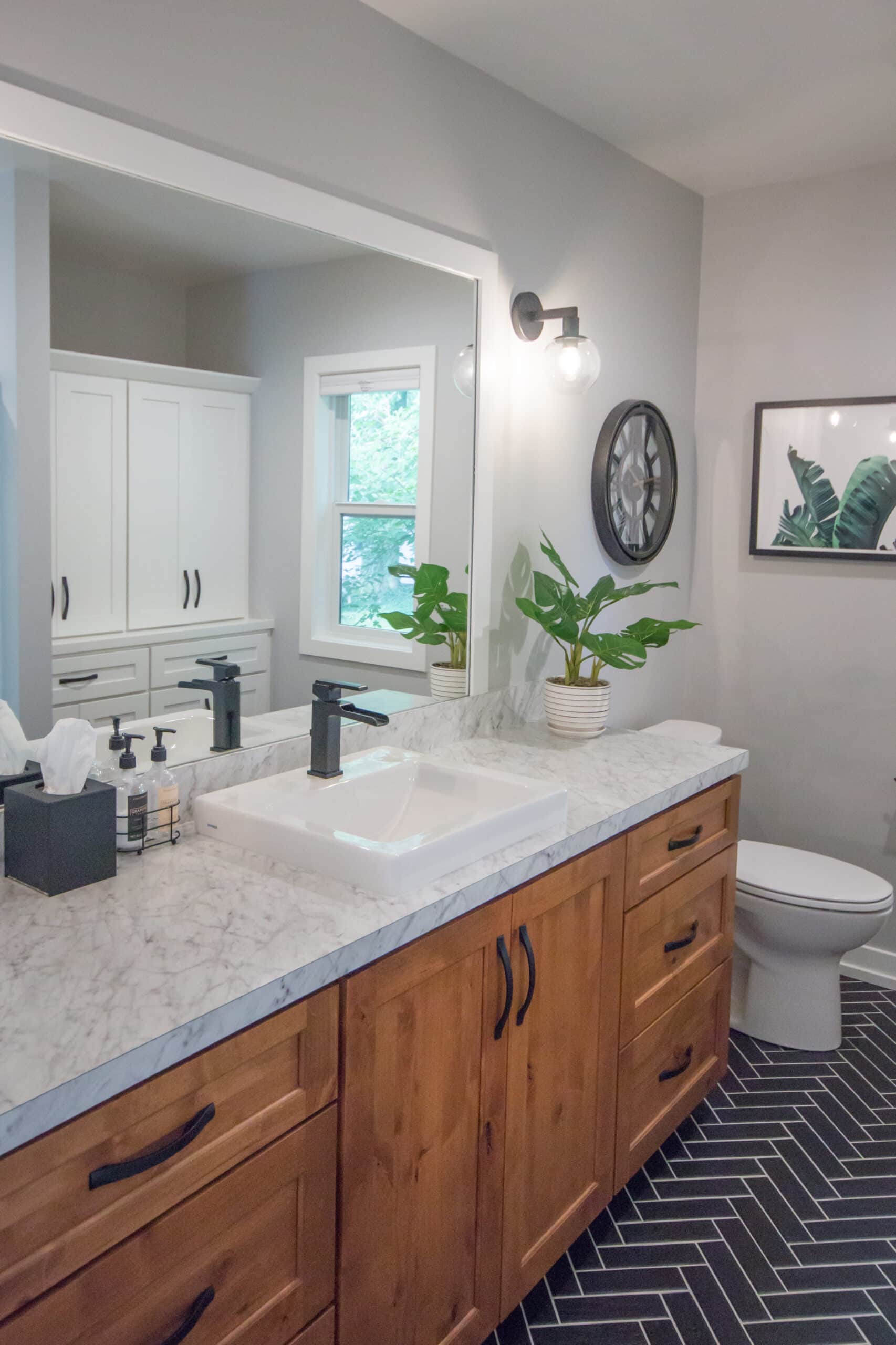 Bathroom with wooden vanity, white countertop, and green plants near mirror.