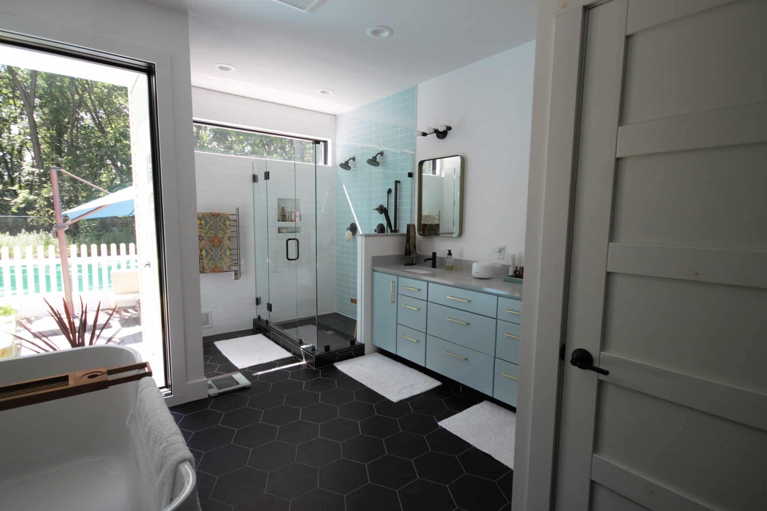Contemporary bathroom with glass shower, light blue vanity, and black hex tile flooring.