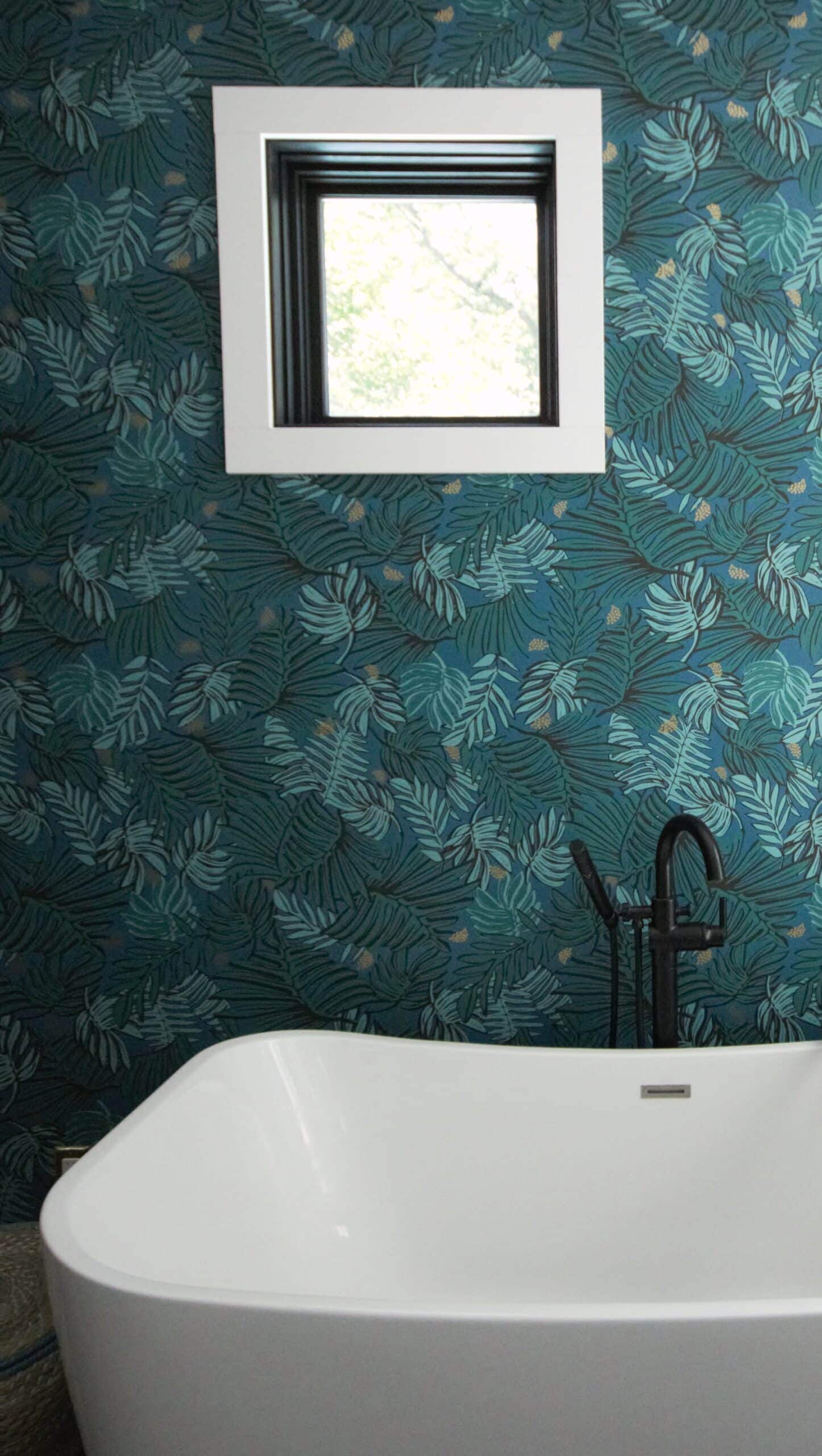 Bathroom with a square window and tropical leaf wallpaper.