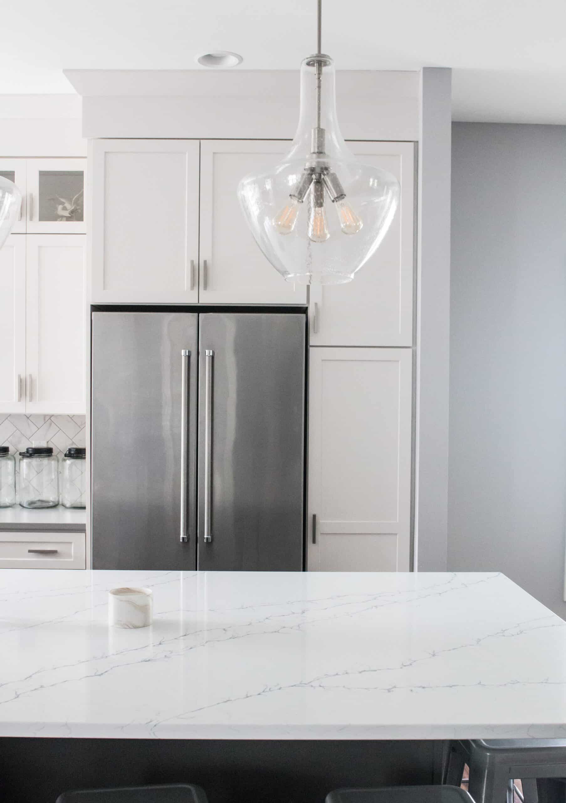 Contemporary kitchen with white cabinets, stainless steel refrigerator, and glass pendant light.