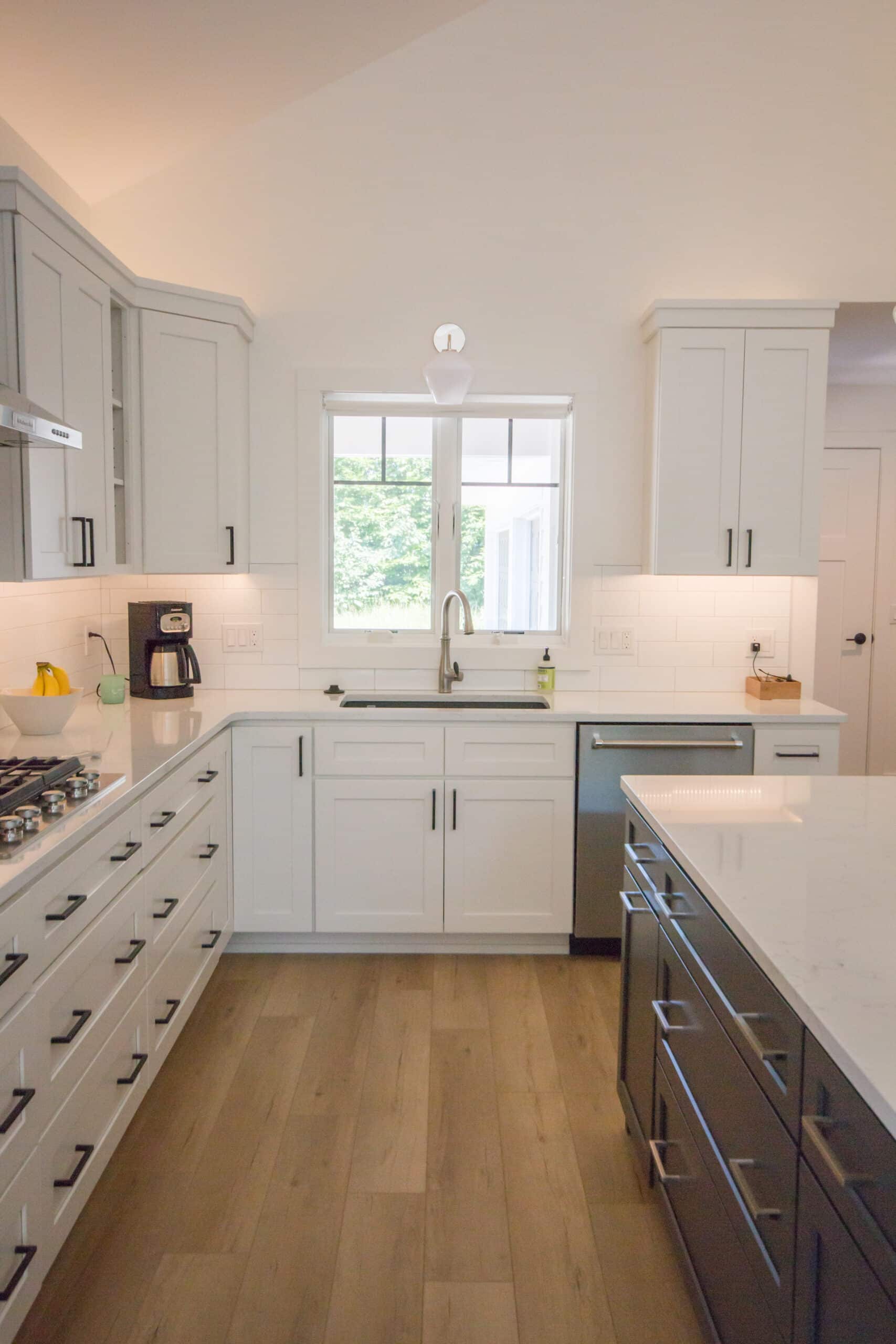 Bright modern kitchen with white cabinets, island, and large window.