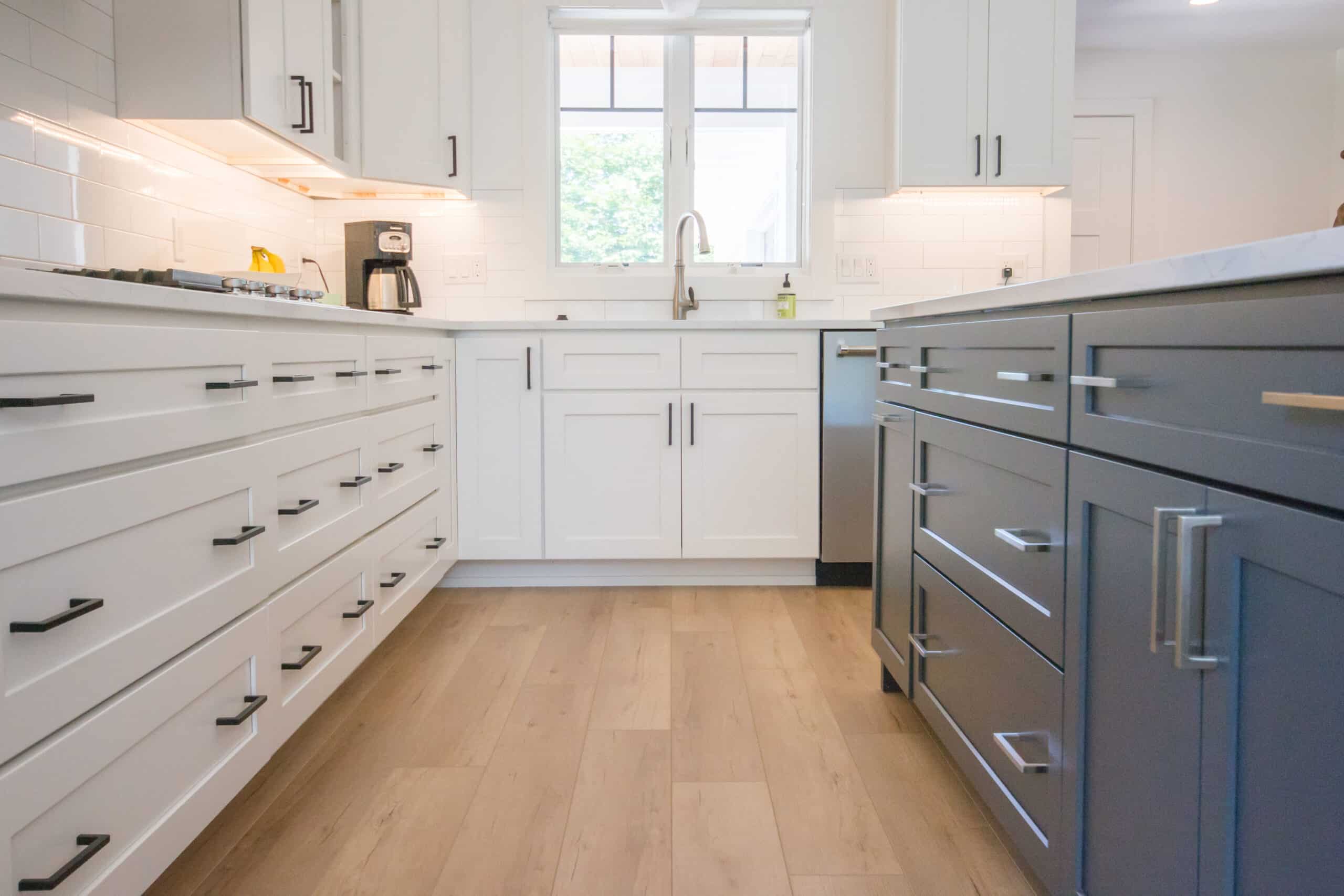Contemporary kitchen with white cabinets, blue island, and wooden flooring.