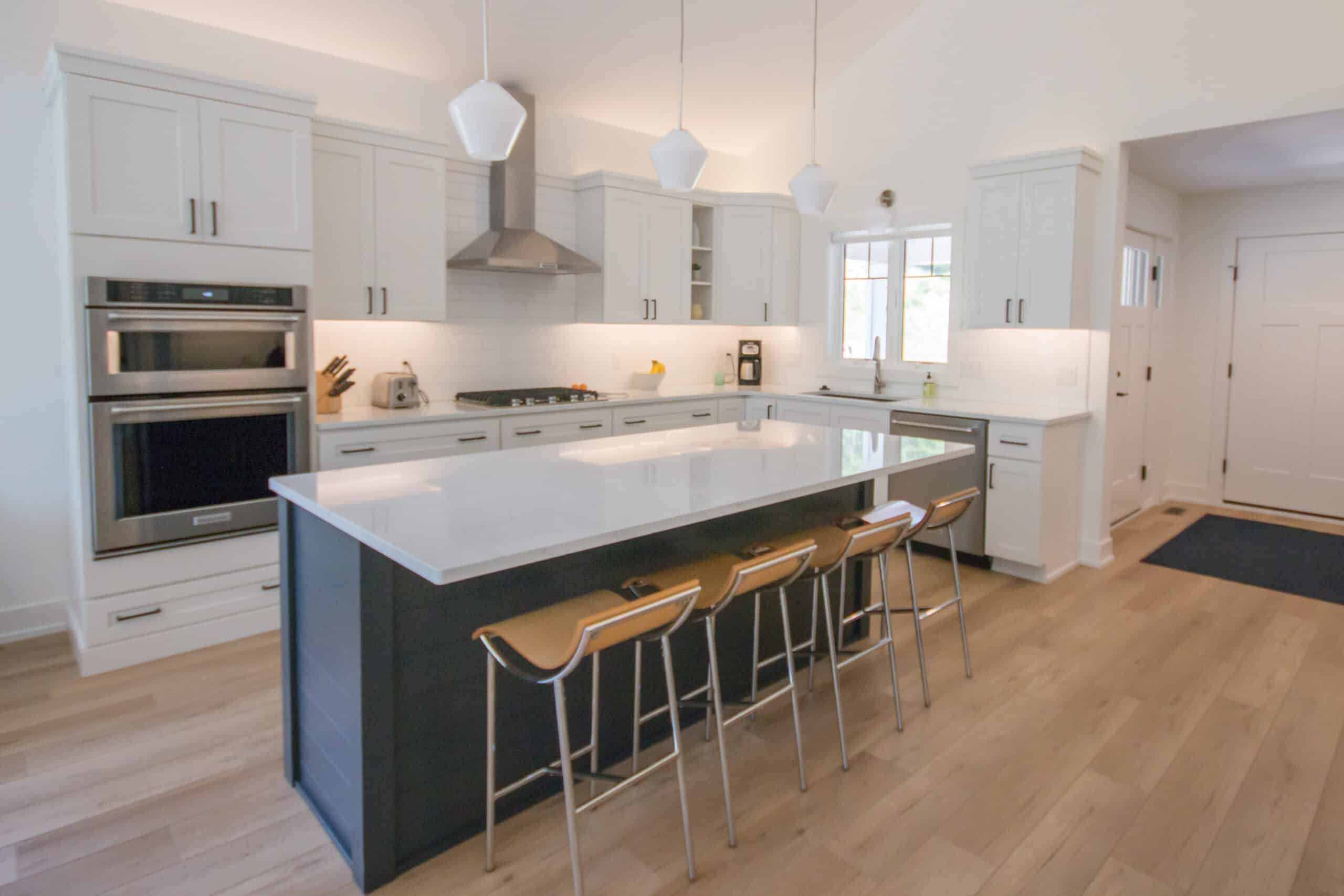 Contemporary kitchen with white cabinets, island, bar stools, and stainless steel appliances.