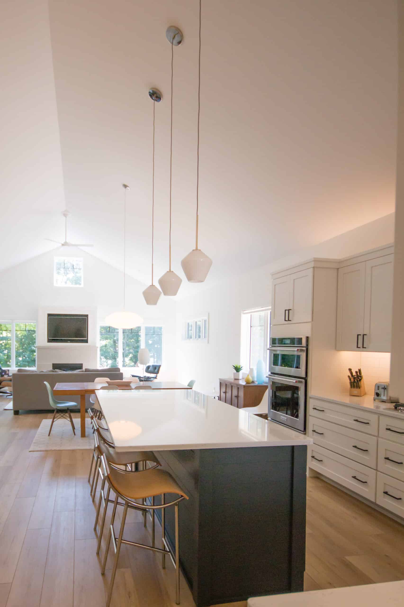 Bright modern kitchen with white cabinets and island, pendant lights, and open living space.