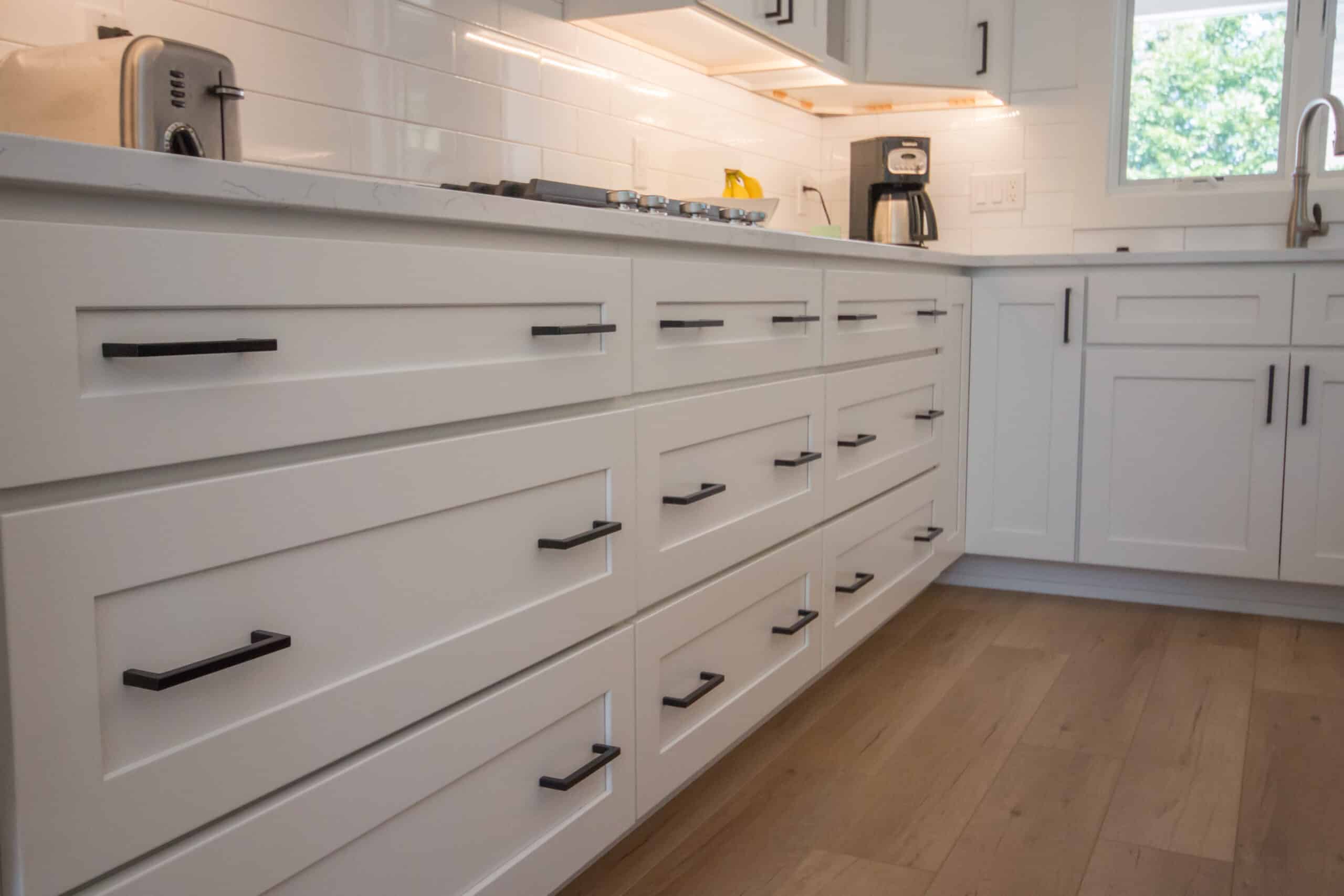 Contemporary white kitchen cabinets with black handles and wooden flooring.