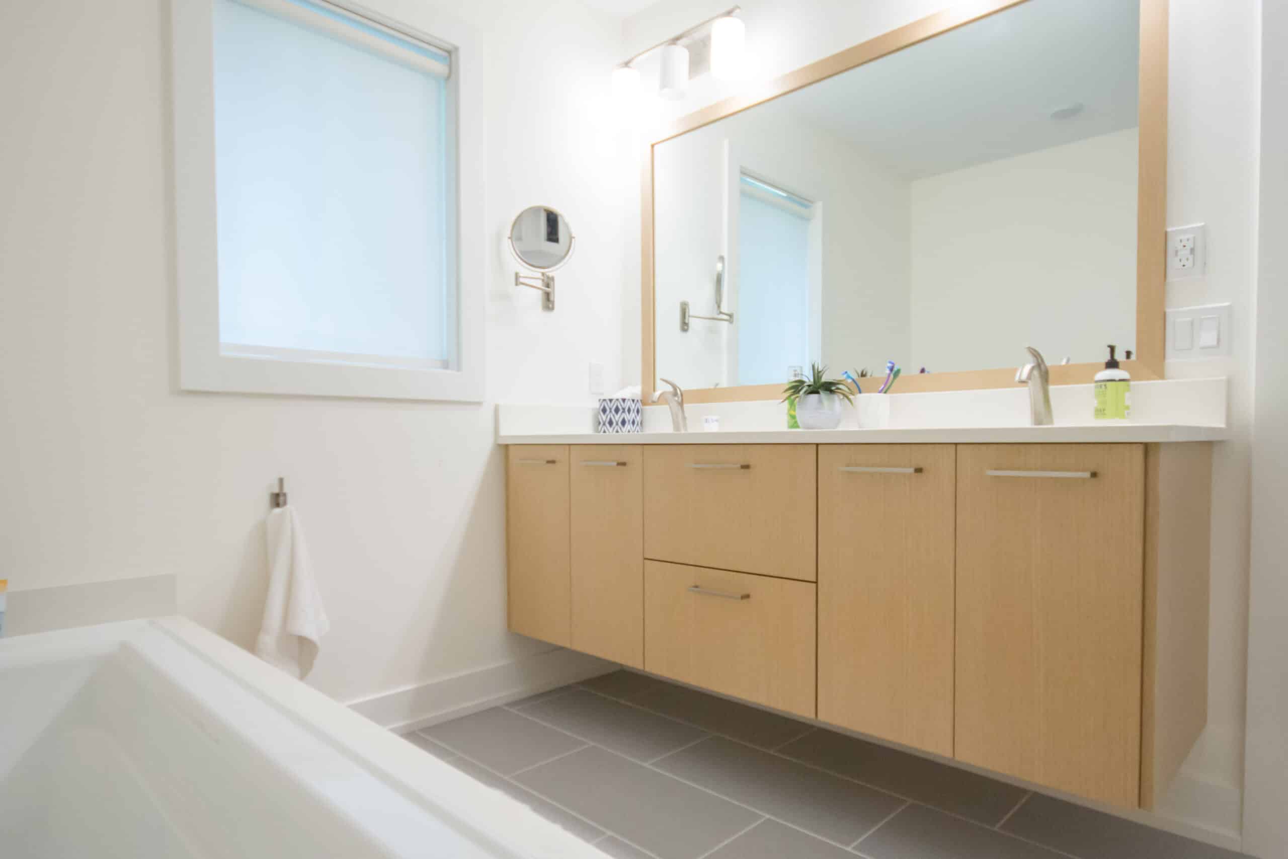 Bright bathroom with large mirror, wooden vanity, and white walls.