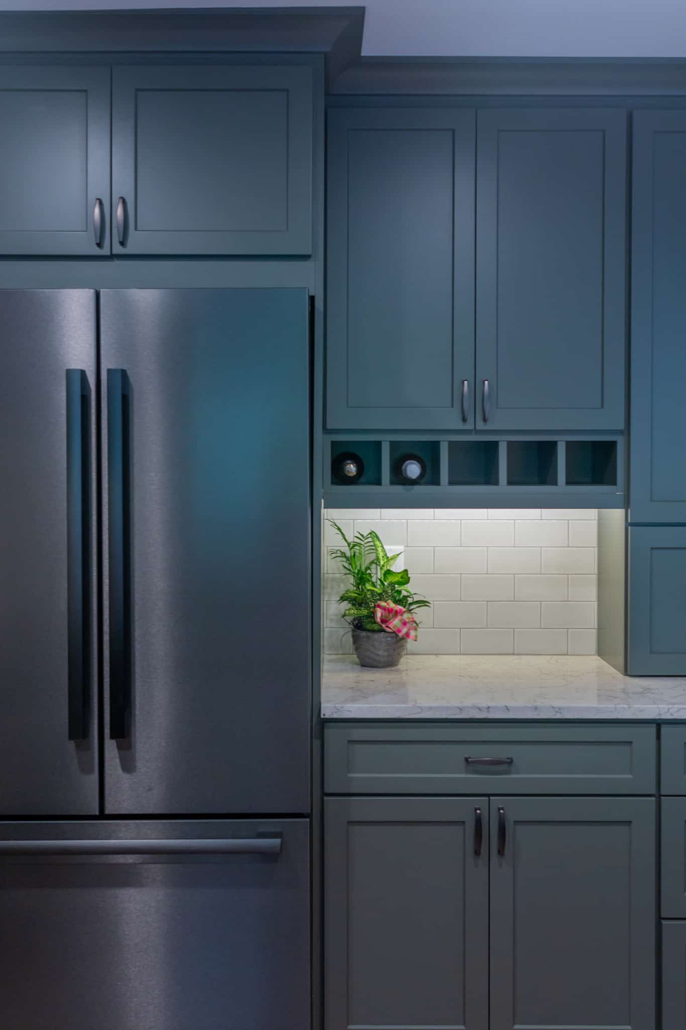 Modern blue kitchen cabinets with stainless steel refrigerator and white tiled backsplash.