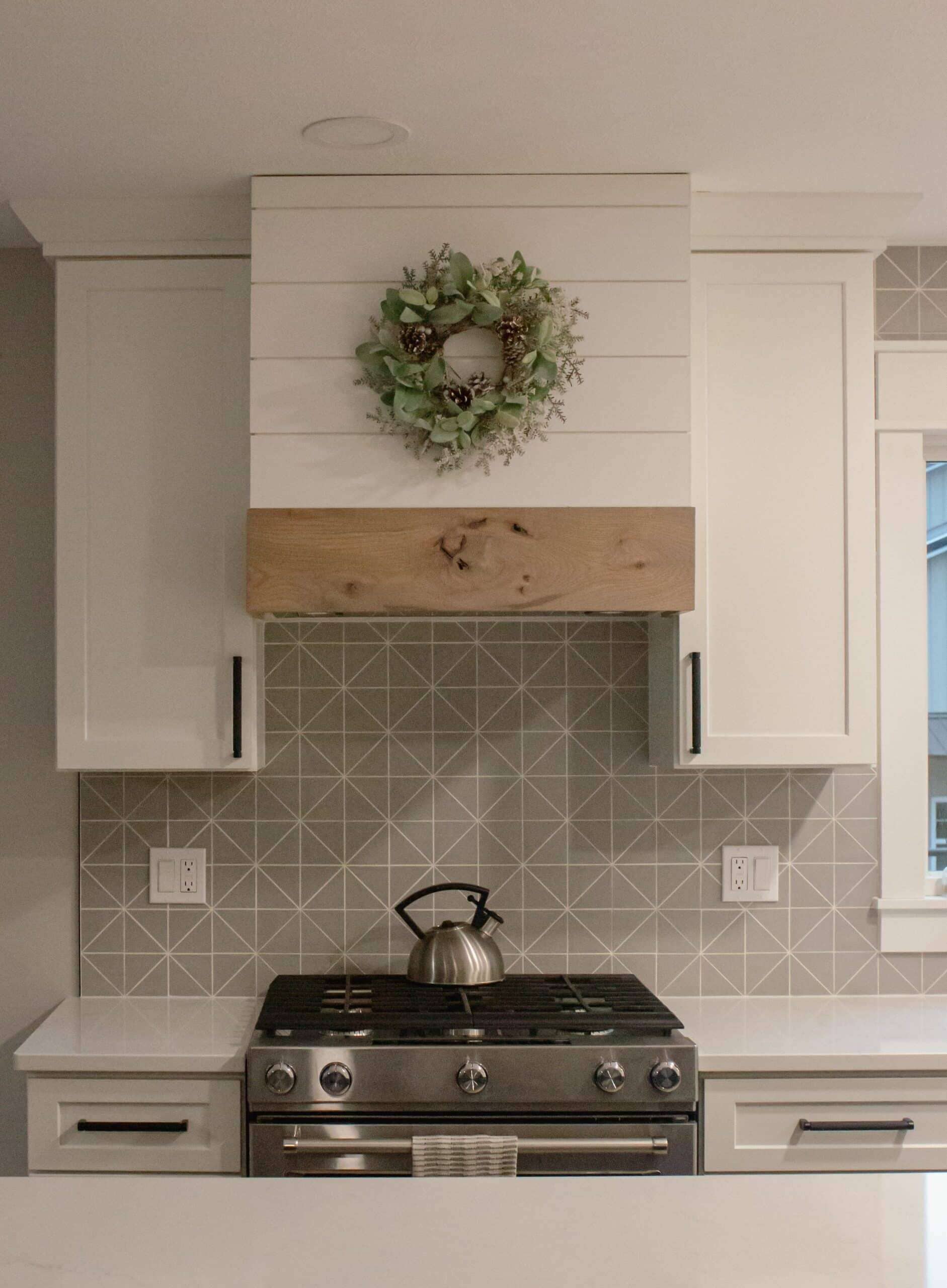 Kitchen with white cabinets, geometric backsplash, and a decorative wreath above the stove.