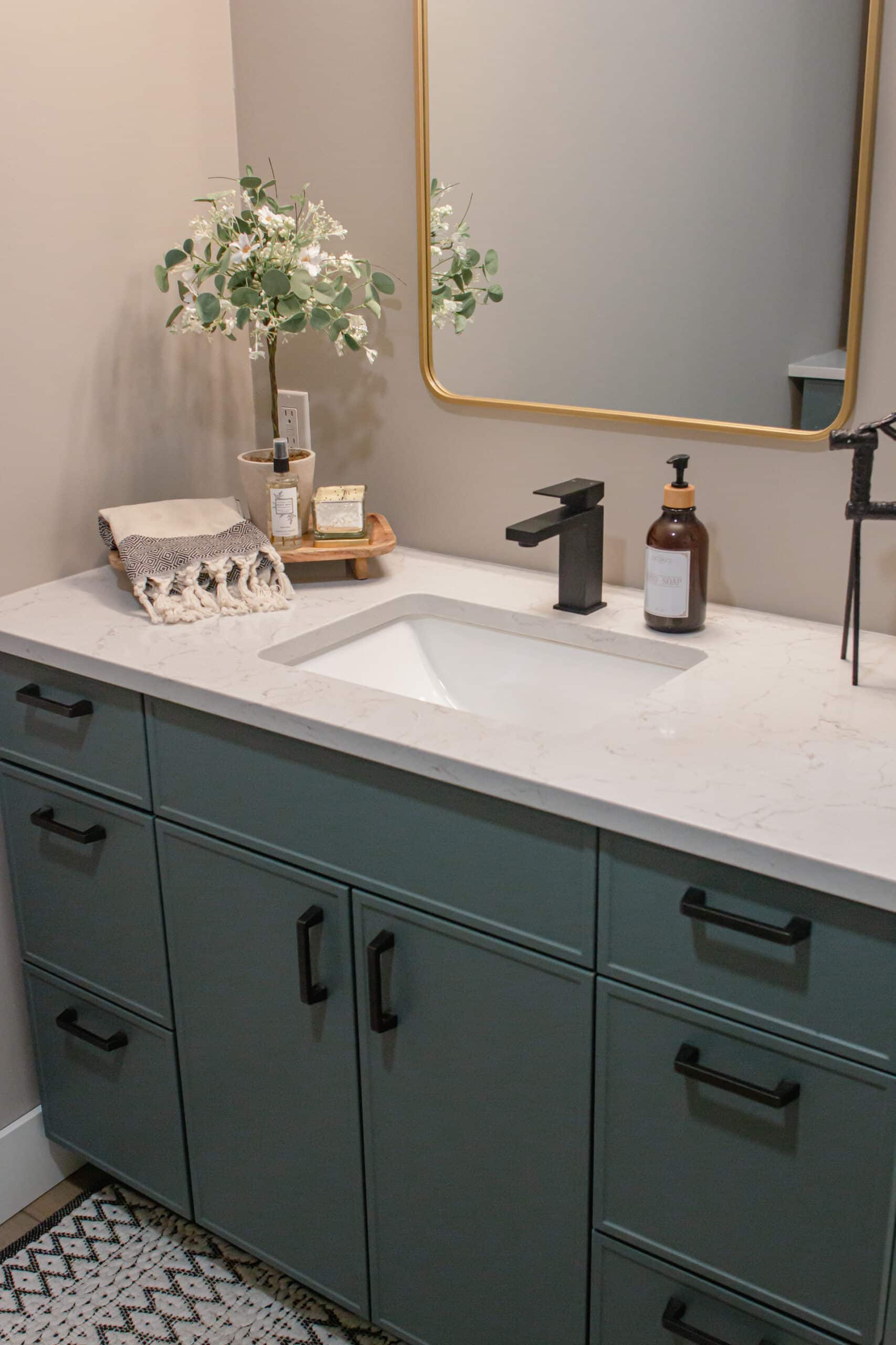 Bathroom vanity with green cabinets, white countertop, black faucet, and decorative mirror.
