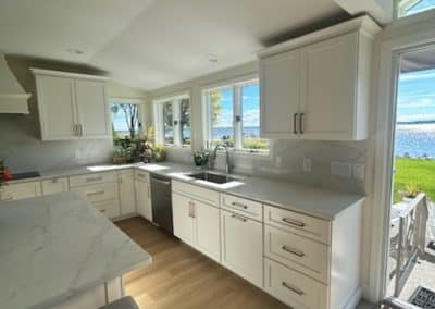 Bright modern kitchen with white cabinets and large windows overlooking water.