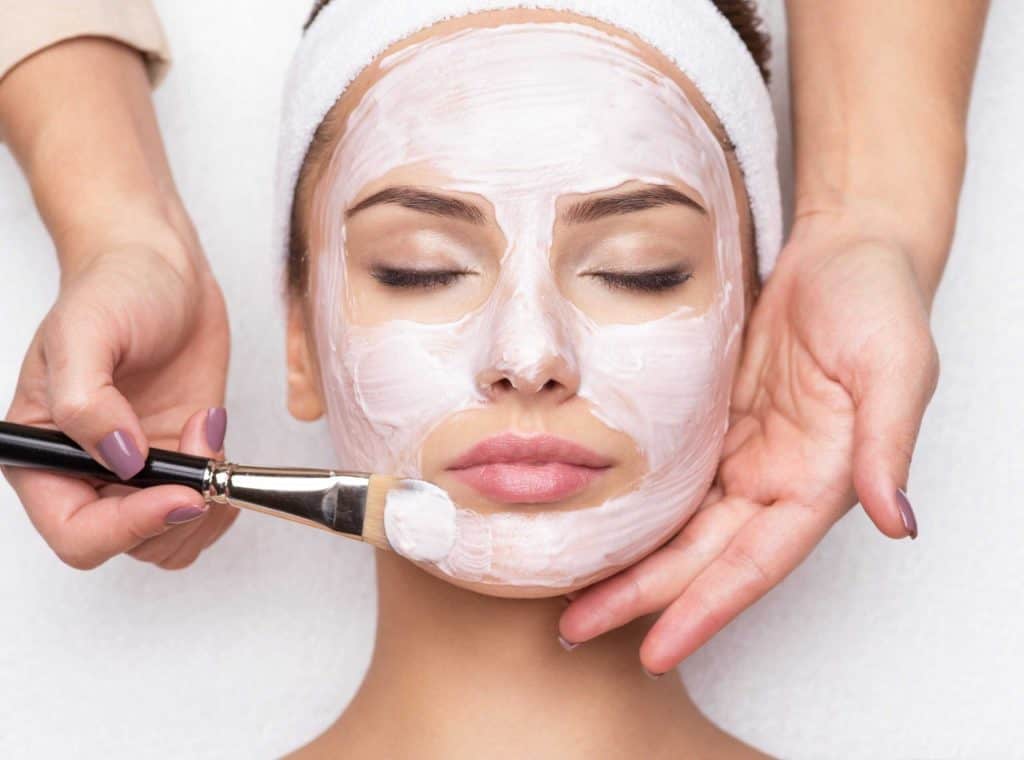 Woman receiving facial with white cream at beauty spa.