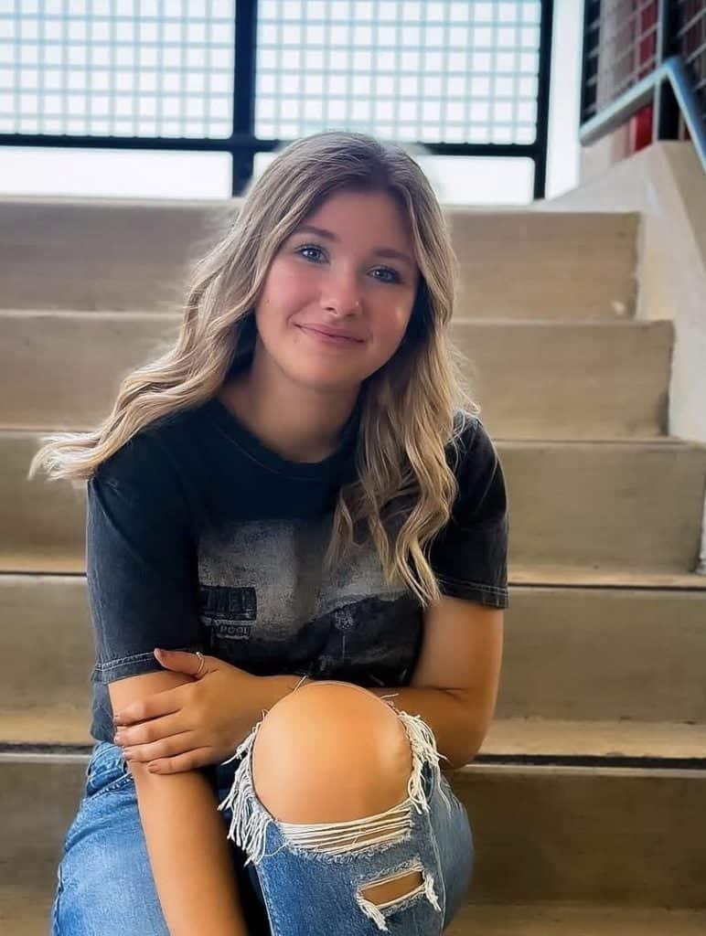 Young woman with blonde hair sitting on stairs at spa, smiling.