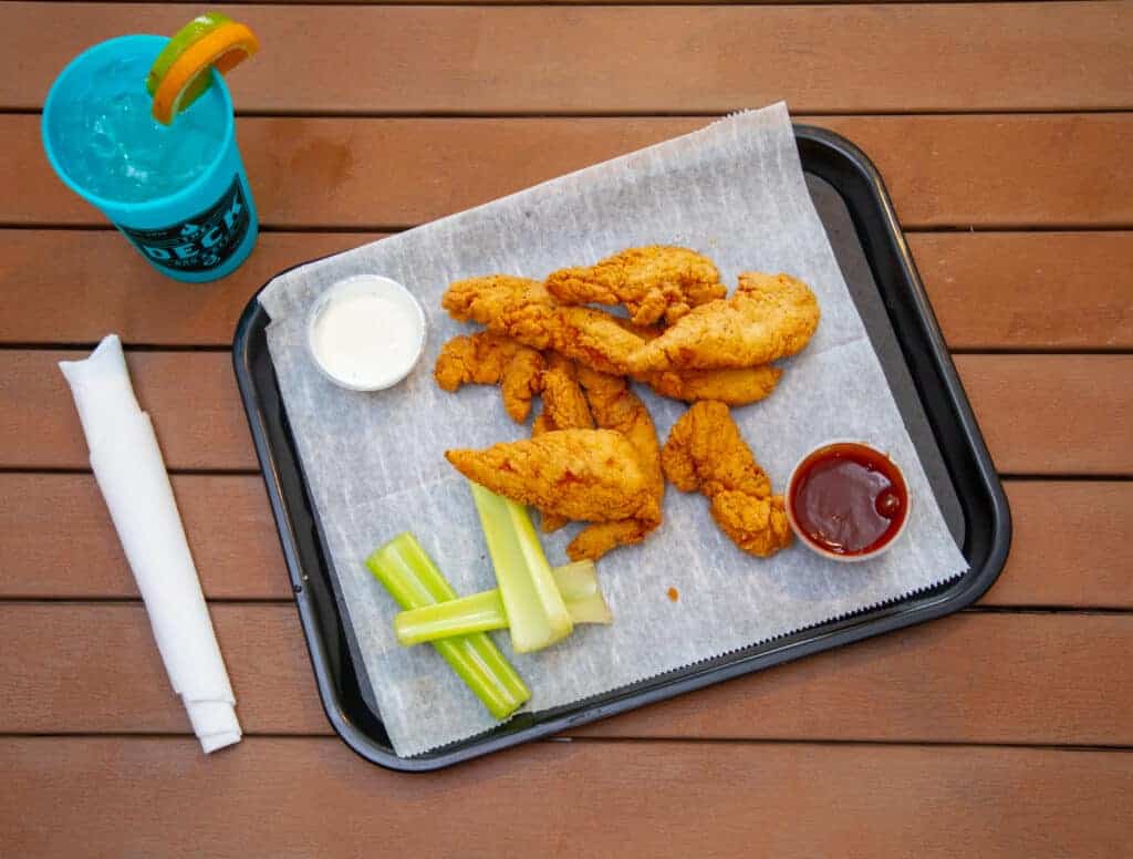 Crispy chicken strips with celery sticks and dipping sauces on a tray.