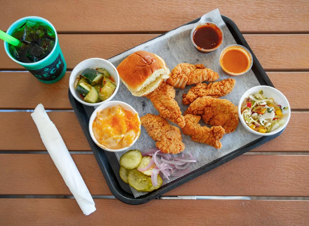 Crispy chicken strips with sides, drink, and dipping sauces on a tray.
