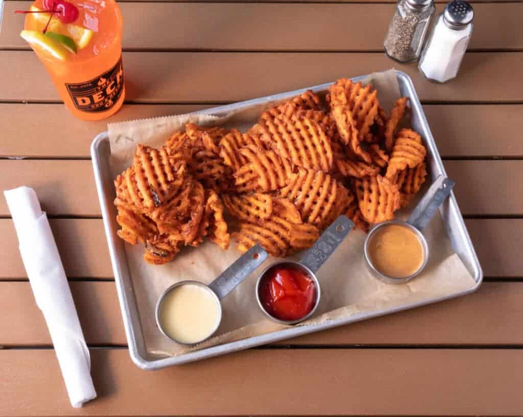 Crispy waffle fries with three dipping sauces on a metal tray.