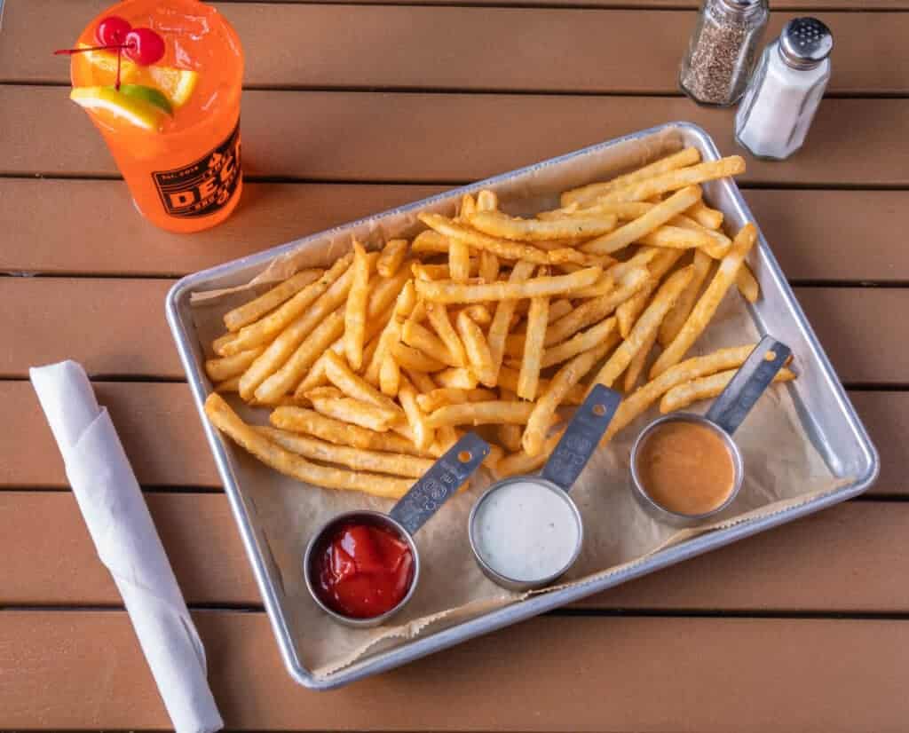 Crispy French fries with ketchup, ranch, and barbecue sauces on a metal tray.