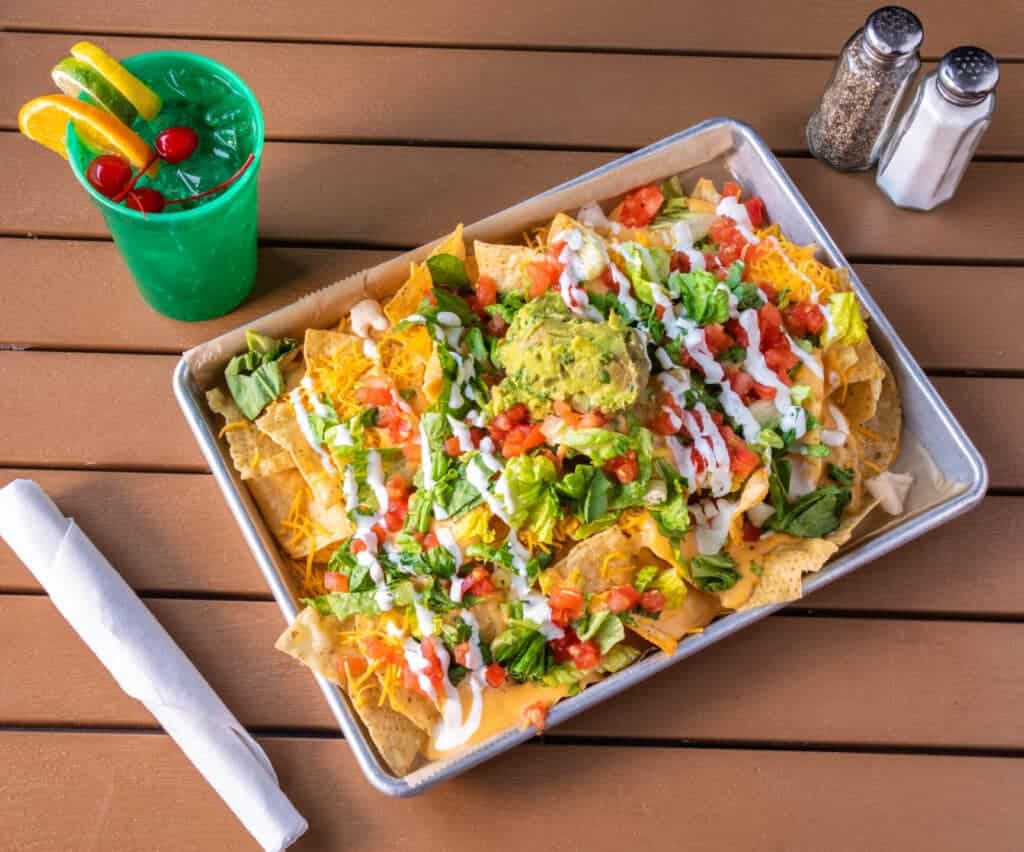 Plate of loaded nachos with lettuce, cheese, guacamole, and salsa.