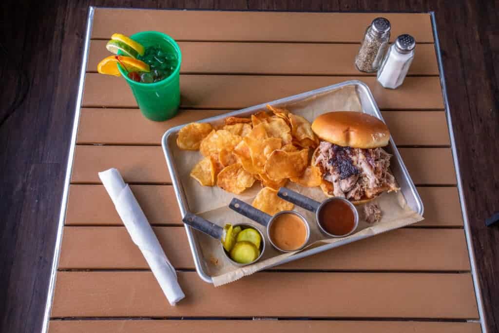 Pulled pork sandwich with chips, pickles, and drinks on a tray.