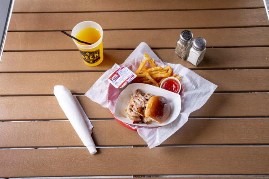 Pulled pork slider with fries, ketchup, and a drink on a wooden table.