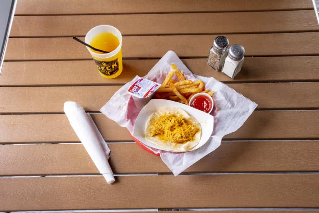 Chicken taco with fries, cheese, and condiments on a wooden table.