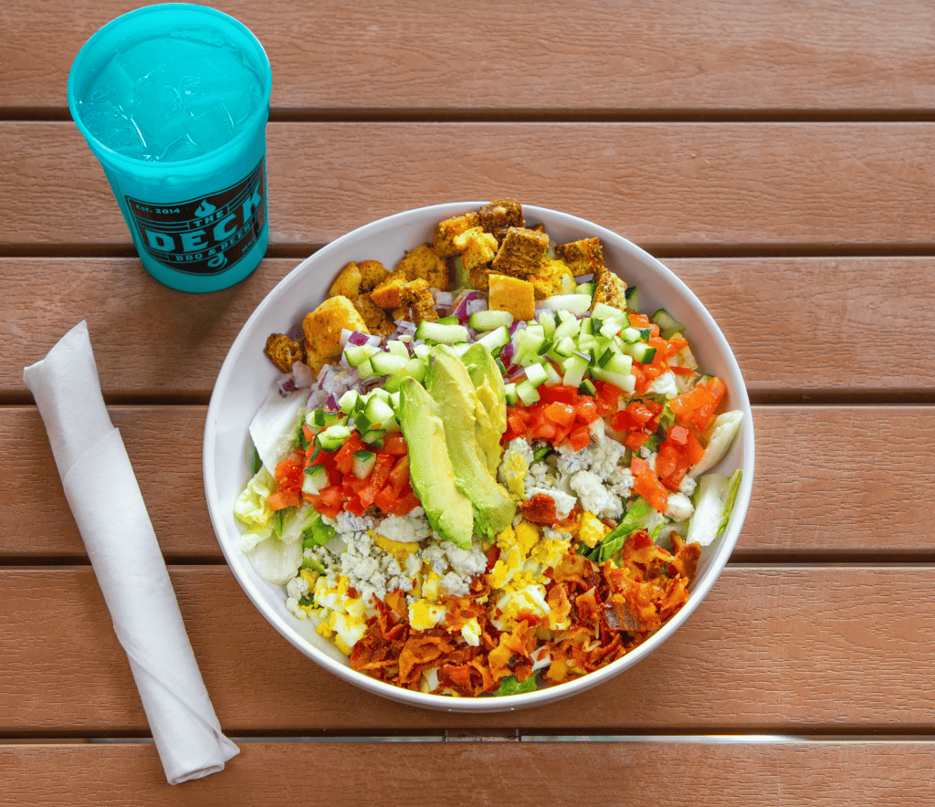 Colorful Cobb salad with avocado, tomatoes, bacon, and croutons on a wooden table.