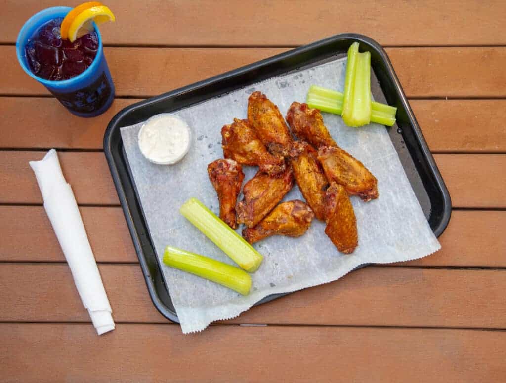 Smoked chicken wings with celery sticks and dipping sauce on a tray.