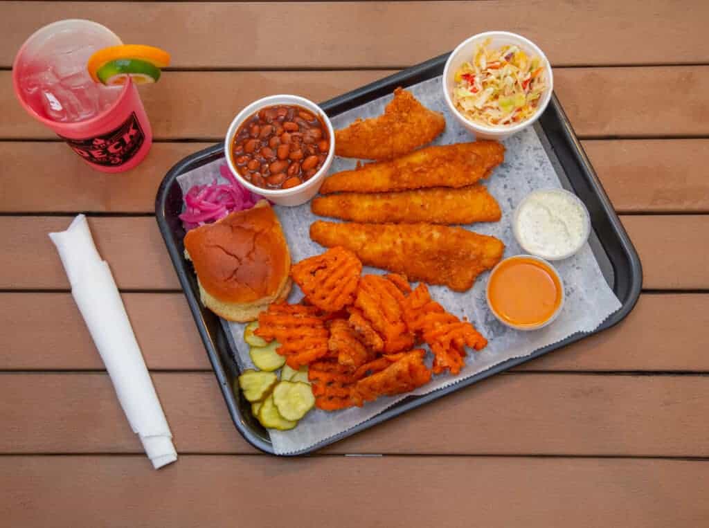 Fish fry platter with coleslaw, baked beans, and fries on a tray.