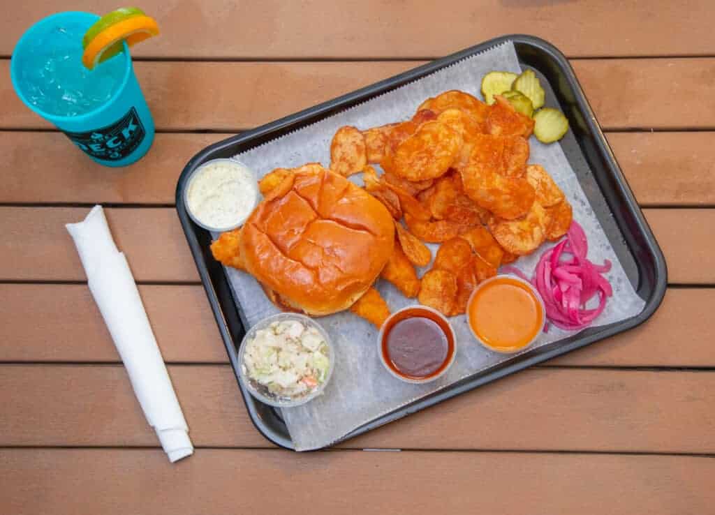 Fried walleye sandwich with pickles, onion, and sauces on a tray.