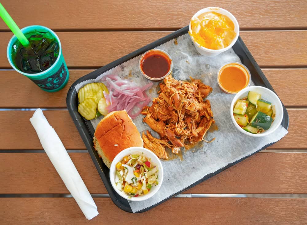Pulled smoked chicken with sides and drinks on a tray.