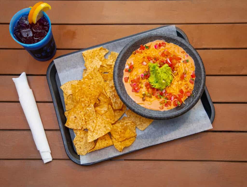 Queso cheese dip with tortilla chips and a soda on a wooden table.