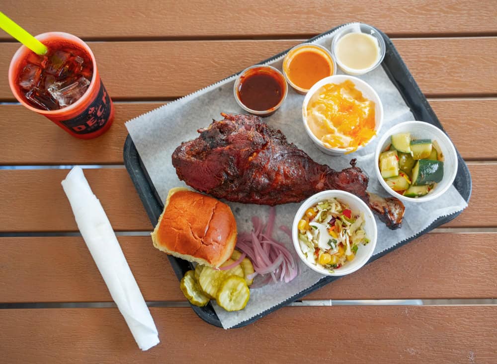 Smoked turkey leg with pickles, bread, onions, and sauces on a tray.