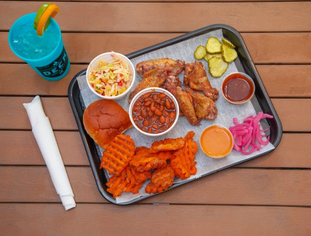 Smoked chicken wings with sides of coleslaw, pickles, baked beans, waffle fries, and sauces.