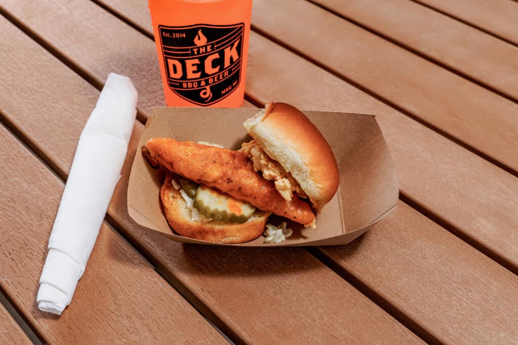 Crispy fried chicken sandwich with pickles in a bun on a wooden table.