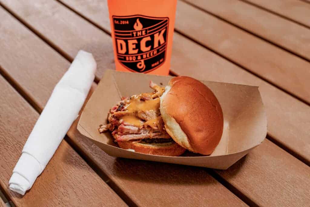 Burger with cheese and meat on a bun with a drink in a cup from The Deck.