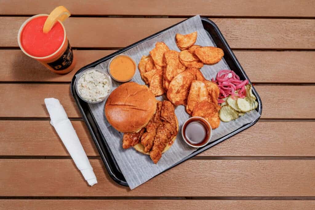 Nashville hot chicken sandwich with sides and drink on a tray.
