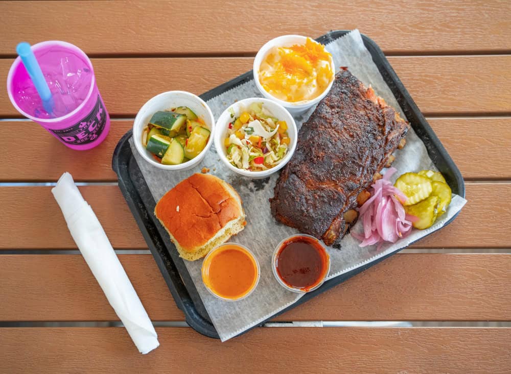 Smoked pork ribs with sides and sauces on a wooden table.