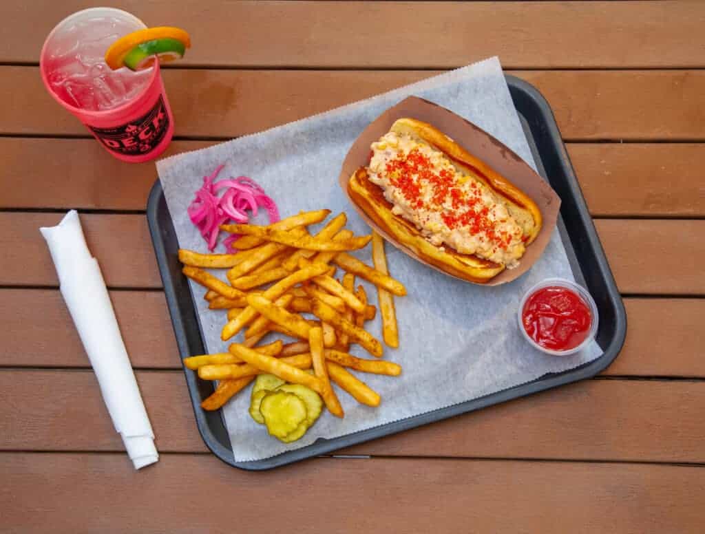 Hot dog with toppings, fries, pickles, and drink on a tray.
