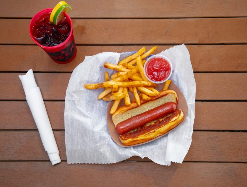Hot dog with fries, ketchup, and a soda on a wooden table.