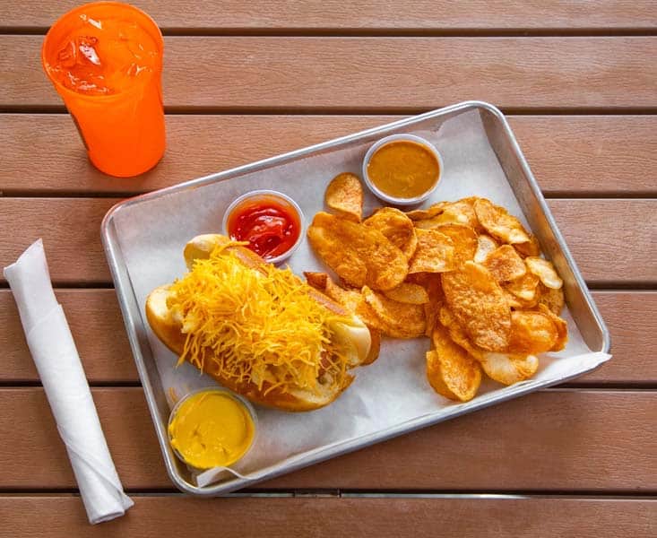 Fish and chips with three dipping sauces and a drink on a wooden table.