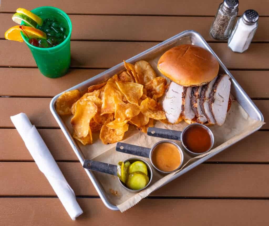 Smoked turkey breast sandwich with chips and barbecue sauce on a tray.