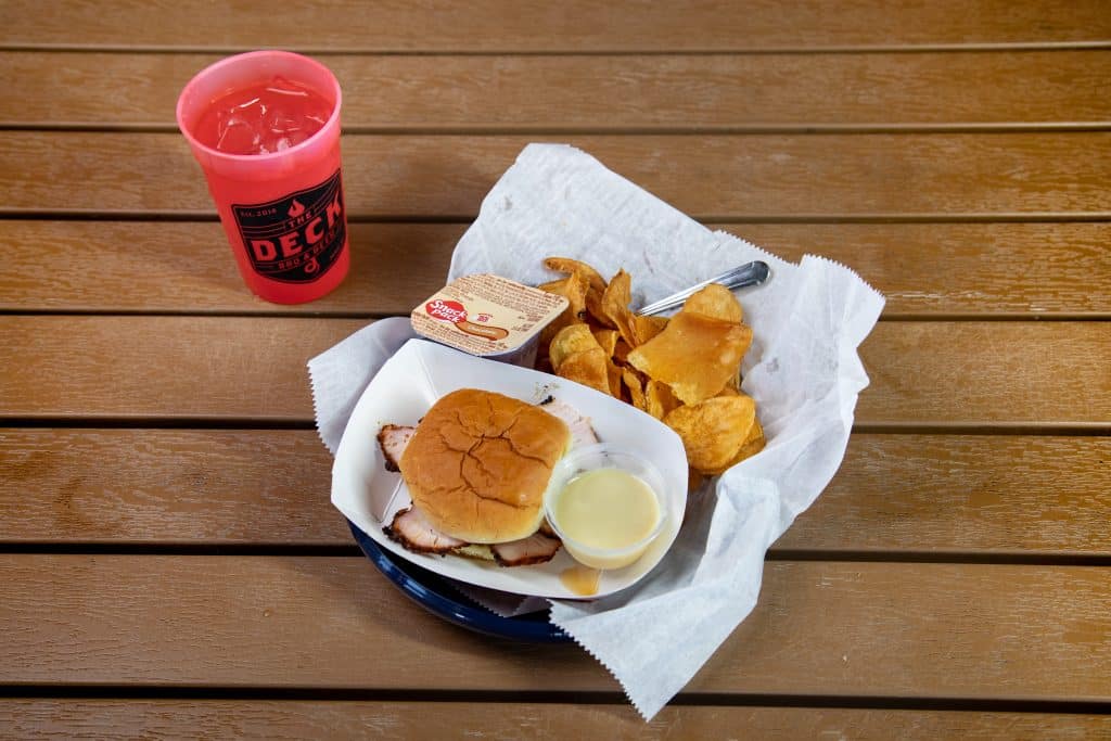 Turkey breast slider with chips, dipping sauce, and drink on wooden table.
