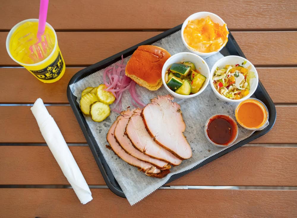 Smoked turkey breast slices with pickles, bread, and sides on a tray.