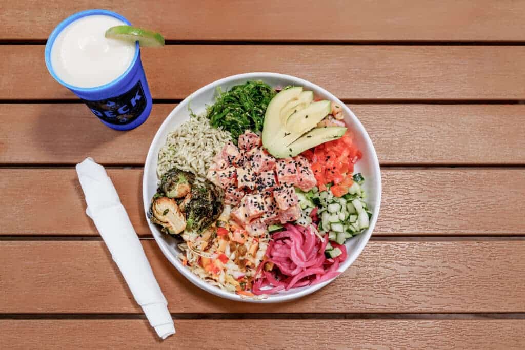 Colorful tuna poke salad with fresh vegetables and rice, served with a drink on wooden table.