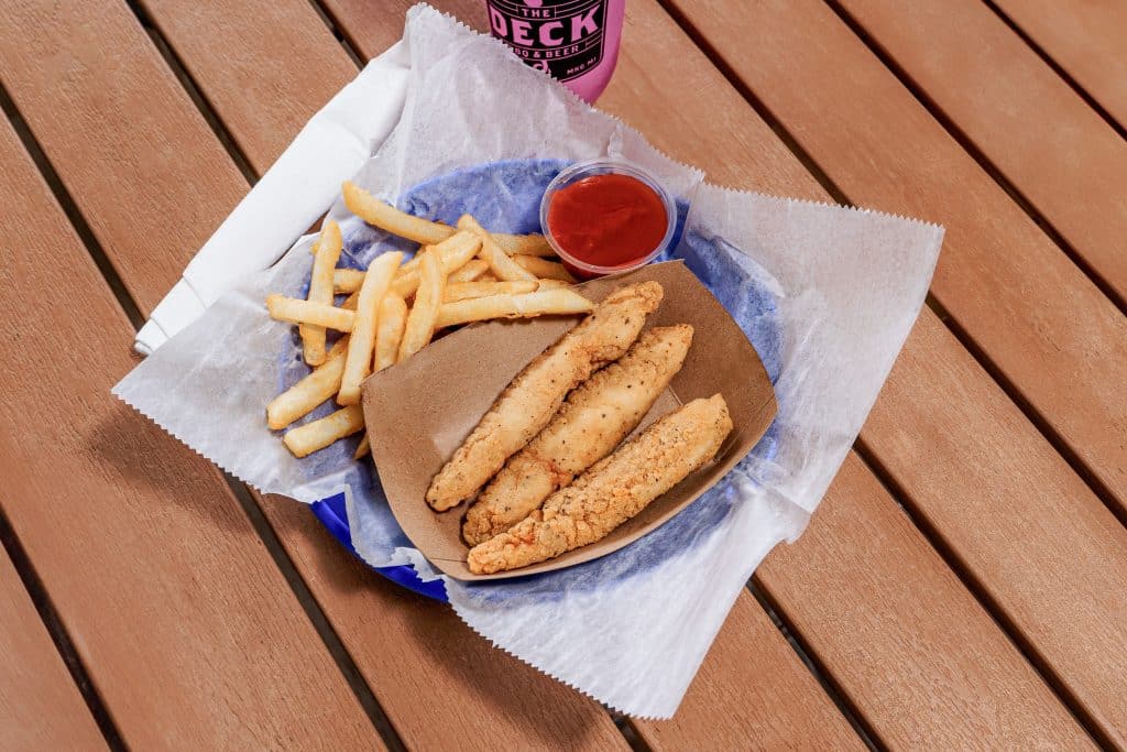 Crispy chicken tenders with fries and dipping sauce on a wooden table.
