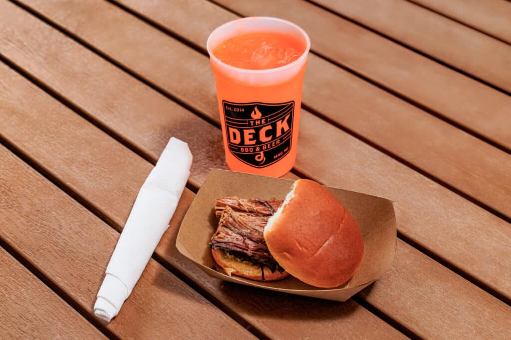 Barbecue sandwich, drink, and napkin on wooden table.