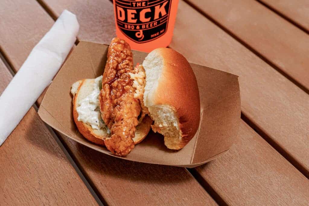 Fried chicken sandwich with honey and a drink on a wooden table.