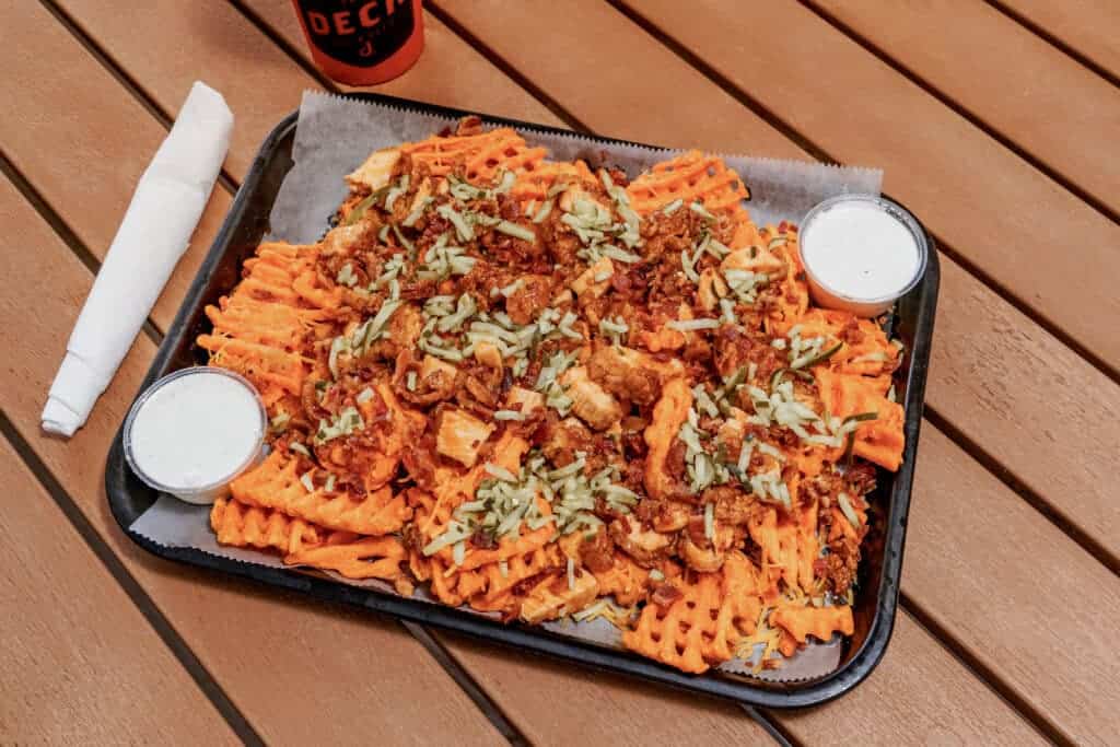 Loaded waffle fries with cheese, chicken, and toppings on a tray.
