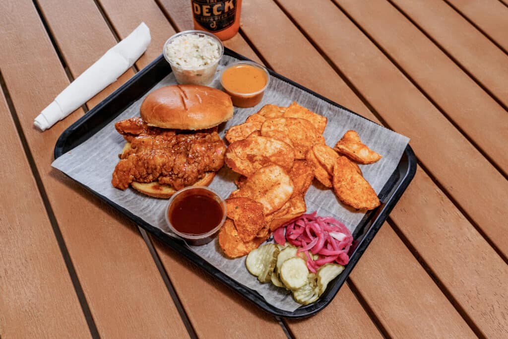 Fried chicken sandwich with potato chips, pickles, and sauces on a tray.