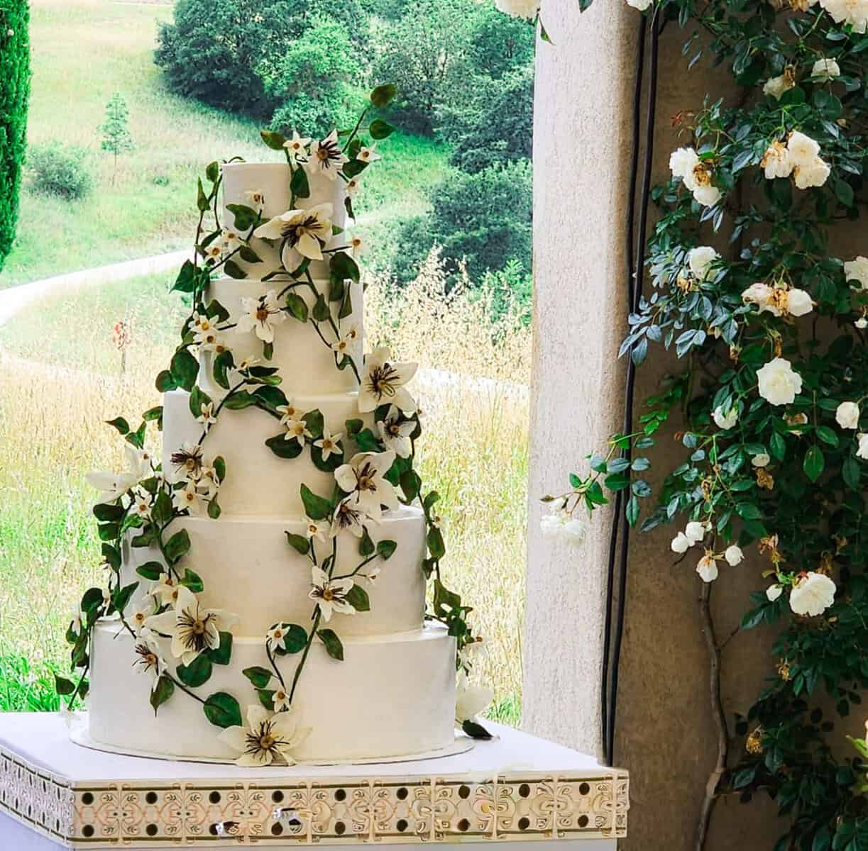 White tiered wedding cake with sugar clematis flowers and greenery at Castello di Reschio in Siena, Tuscany, Italy, planned by Todd Events.